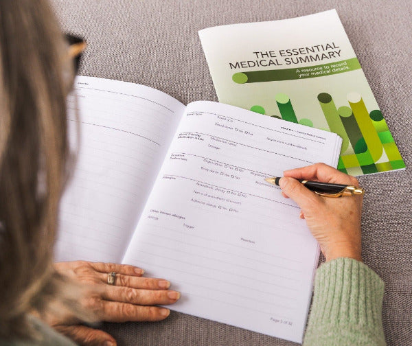 Person filling out a medical form with an 'Essential Medical Summary' guide on a couch.
